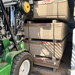 Usługi Stolarskie Ksawier Daniel Milewczyk - Wózek widłowy transportuje palety z płytami drewnianymi Eurodekor marki Egger w Luzinie. Widoczne opakowania z informacjami o produkcie.