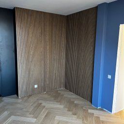 Usługi Stolarskie Ksawier Daniel Milewczyk - Drewniane lamele ścienne w narożniku pokoju z parkietem w jodełkę, oświetlenie sufitowe w kształcie okręgu, ściany pomalowane na granatowo i niebiesko.