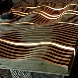 Falista, podświetlana konstrukcja z drewnianych listew, prawdopodobnie element dekoracyjny lub prototyp, z widocznym zasilaczem i okablowaniem.