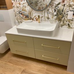 Usługi Stolarskie Ksawier Daniel Milewczyk - Nowoczesna łazienka z szafką pod umywalką w odcieniach zieleni, białym blatem i umywalką, złote detale armatury i uchwytów, oraz tapeta w motywy roślinne i zwierzęce.