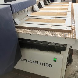 Usługi Stolarskie Ksawier Daniel Milewczyk - Proces obróbki drewnianych elementów na frezarce CNC Morbidelli n100, widoczne ramy drzwiowe w trakcie frezowania, z drobnymi wiórami.