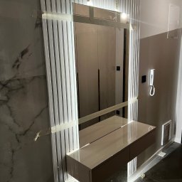 Usługi Stolarskie Ksawier Daniel Milewczyk - Nowoczesna toaletka z lustrem i lamelami dekoracyjnymi w trakcie montażu, zabezpieczona taśmą malarską.