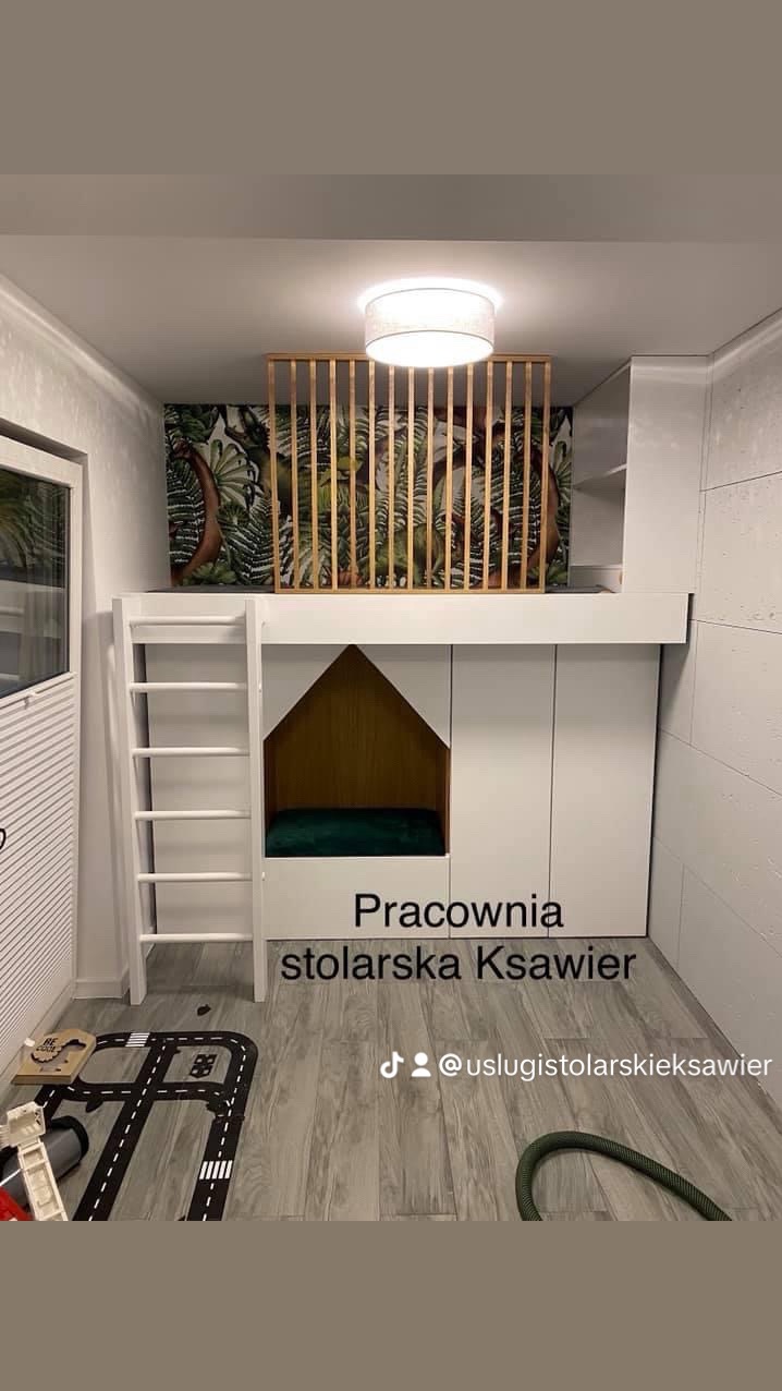 Biała antresola z drabinką i przestrzenią do zabawy dla dziecka, z drewnianą barierką i tapetą w tropikalne liście, widok na podłogę z dywanem imitującym ulicę.