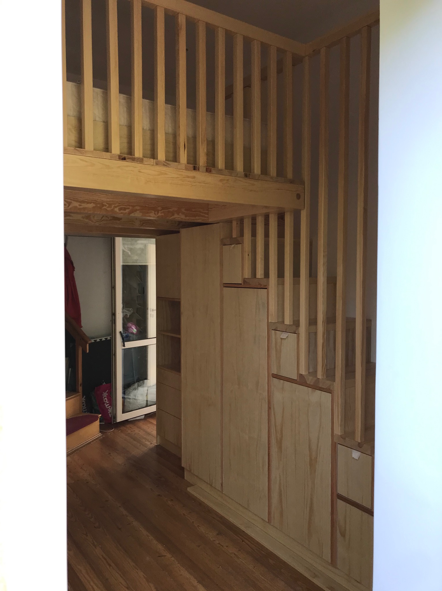 Drewniana antresola z zabudową szaf w Luzinie, widok z dołu ukazujący schody zintegrowane z szafami i barierkę z pionowych szczebli.