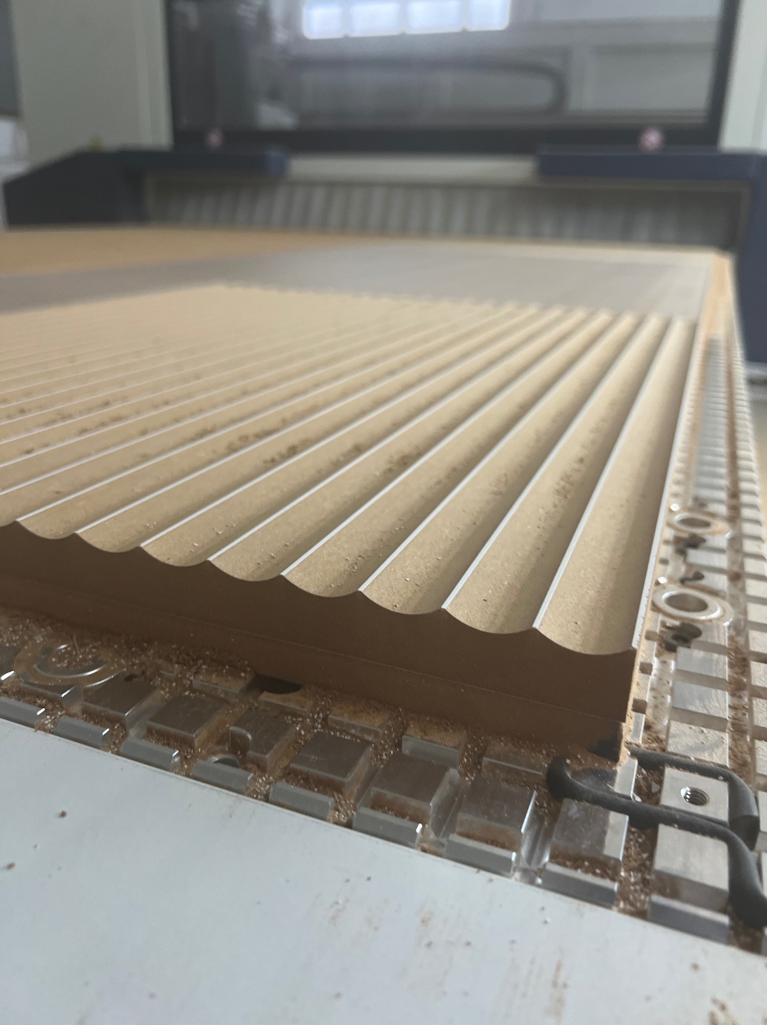 Frezowanie płyty drewnianej na maszynie CNC, widoczne rowki i drobne wióry.