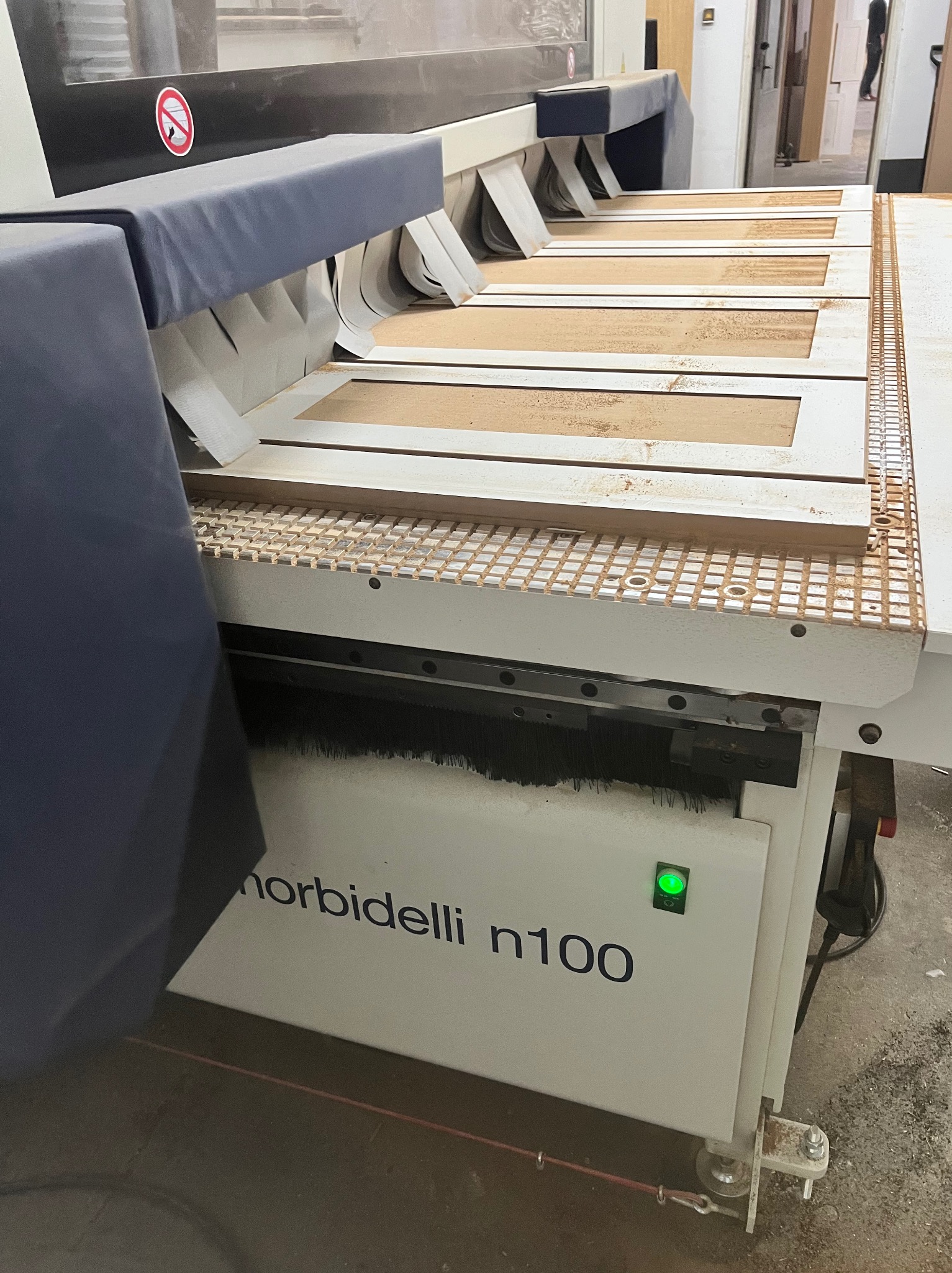 Proces obróbki drewnianych elementów na frezarce CNC Morbidelli n100, widoczne ramy drzwiowe w trakcie frezowania, z drobnymi wiórami.