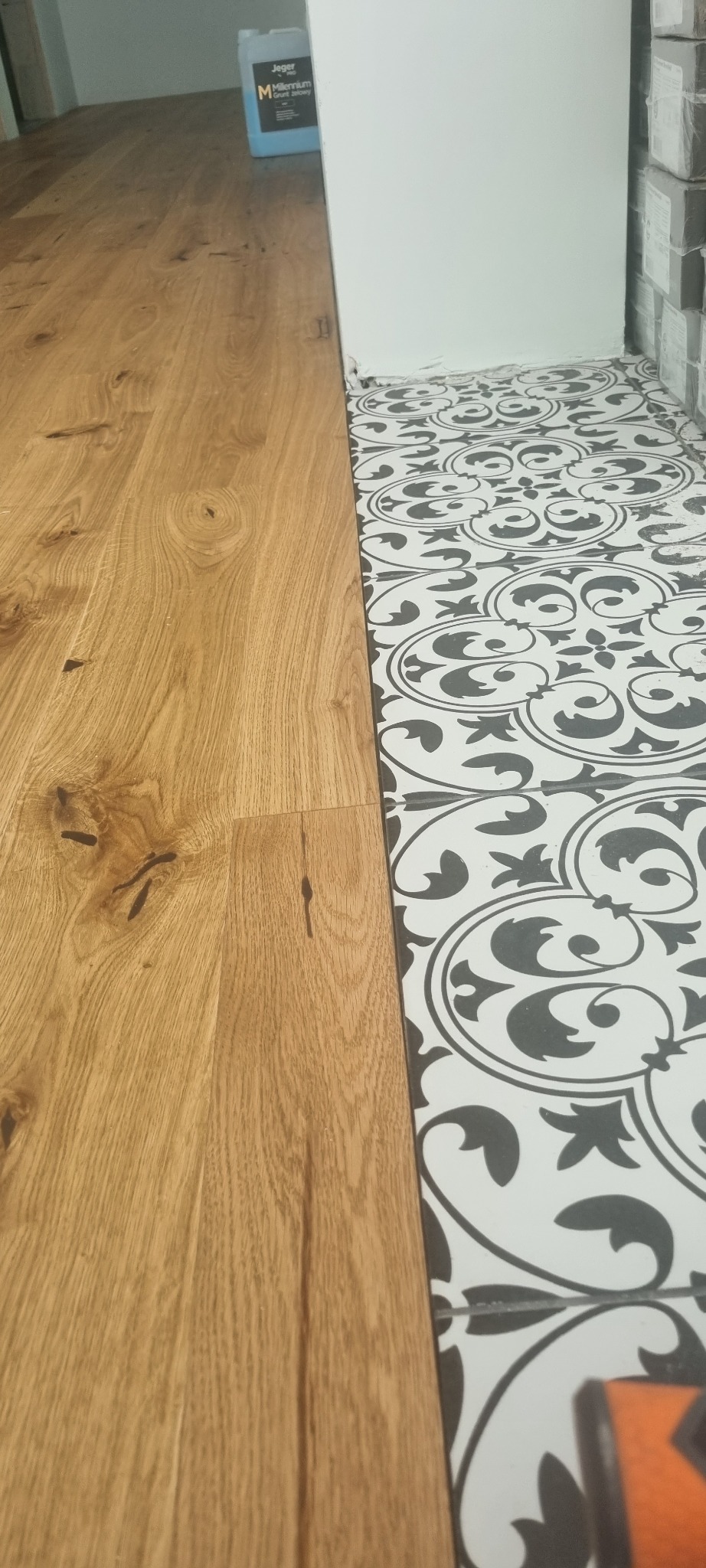 Połączenie jasnego parkietu i dekoracyjnych, czarno-białych płytek podłogowych przy ścianie, widoczny grunt do podłóg.