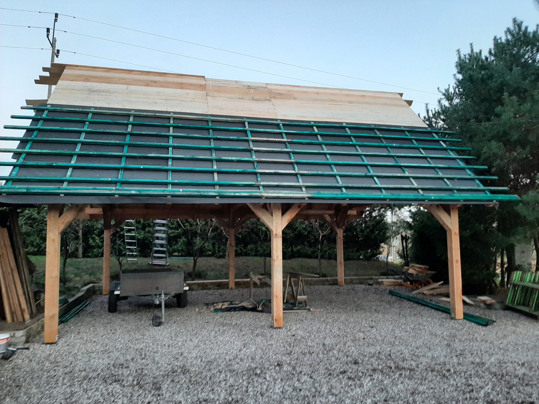 Konstrukcja drewnianej wiaty z zielonymi łatami i podkładem pod dach, częściowo pokryta deskami, widok z zewnątrz w Nowym Barkoczynie.