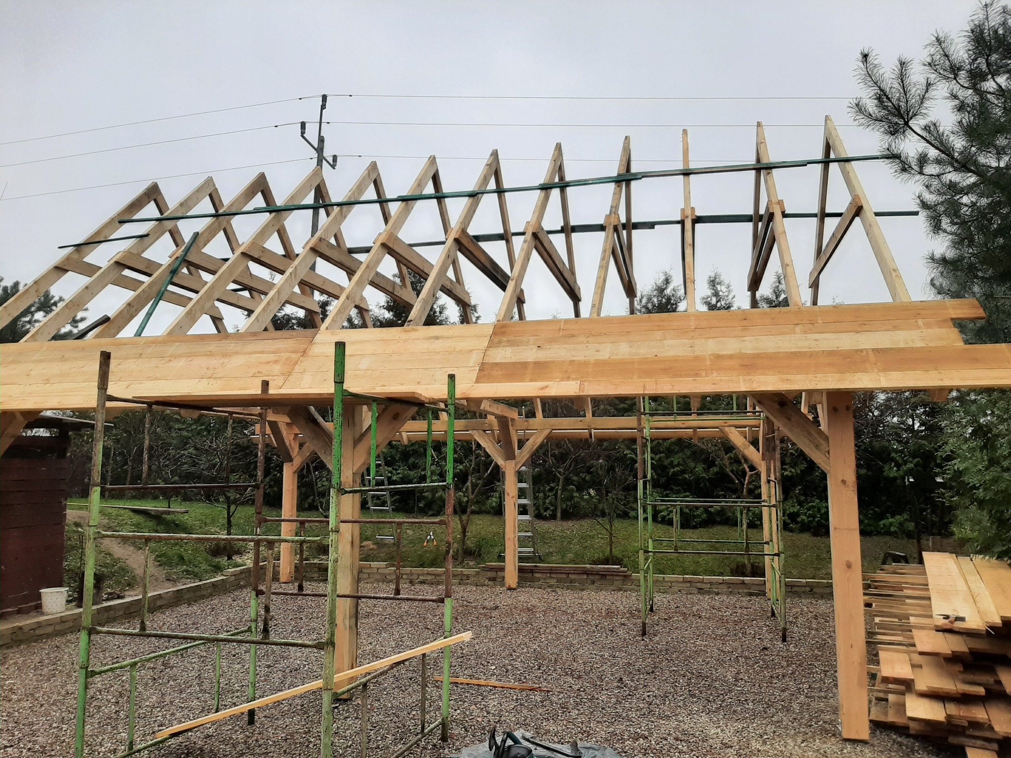 Konstrukcja drewniana z elementami dachu w trakcie budowy, widoczne rusztowania i deski na ziemi.