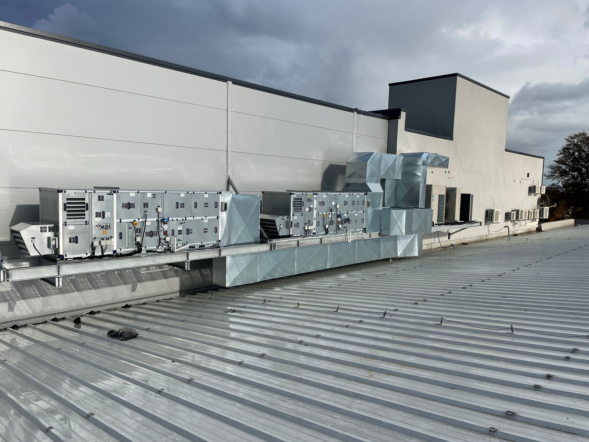 Instalacja wentylacyjna z rurami wentylacyjnymi na dachu budynku przemysłowego, widok z góry, pochmurne niebo w tle.