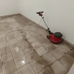 Czerwona szorowarka do podłóg na mokrej, częściowo wyczyszczonej, brudnej podłodze z płytek w pustym pomieszczeniu.