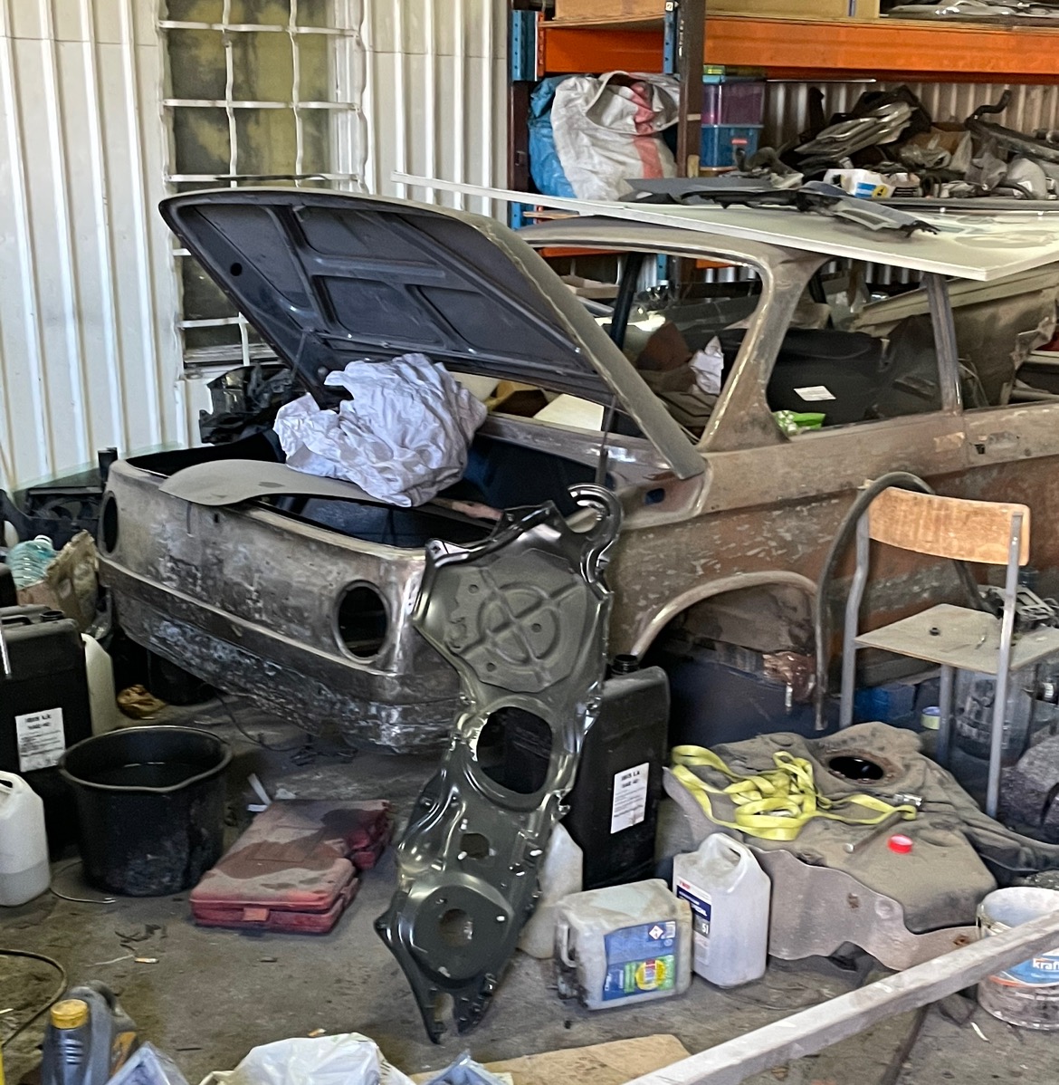 Klasyczny samochód w trakcie renowacji w warsztacie w Łodzi, z otwartą klapą bagażnika i odłożonym elementem karoserii, ukazujący etap prac blacharskich i przygotowania do lakierowania.