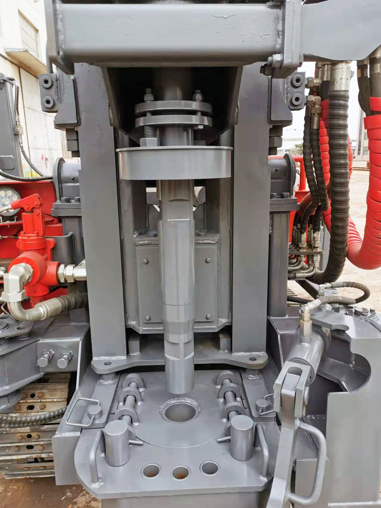 Szczegółowe ujęcie wiertnicy do studni z widocznymi elementami hydraulicznymi, przewodami i mechanizmem wiertniczym, pomalowana na szaro i czerwono.