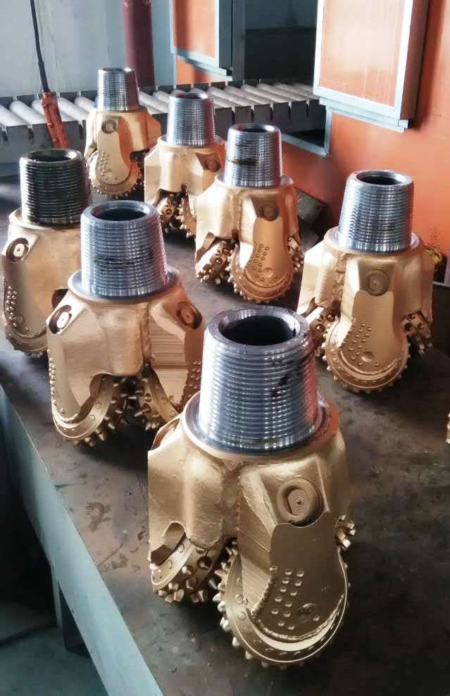 Zestaw nowych, złotych wierteł trójstożkowych z gwintowanymi mocowaniami, ułożonych na metalowym stole w warsztacie.