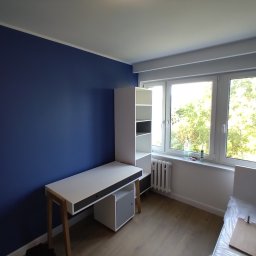 Sas-bud usługi ogólnobudowlane Wojciech Sas - Ściana pomalowana na granatowo w pokoju z białymi meblami, w tym biurko z regałem i grzejnik pod oknem.