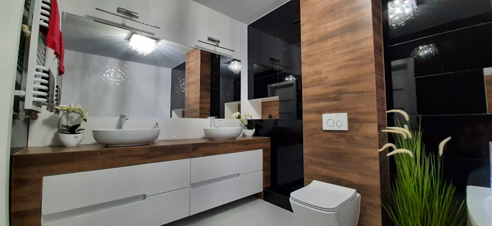 Nowoczesna łazienka z dwoma umywalkami nablatowymi, szafką z drewnianym blatem i białymi frontami, czarnymi i drewnopodobnymi płytkami na ścianach oraz wiszącą toaletą.