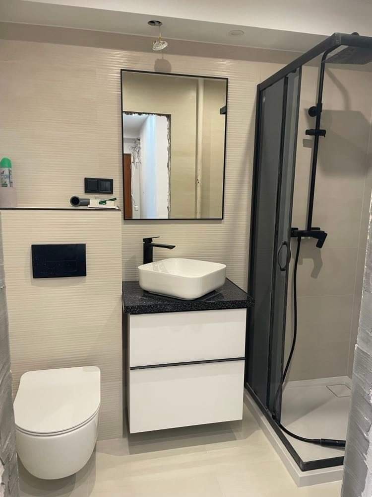 Nowoczesna łazienka z minimalistyczną umywalką nablatową, czarną armaturą i kabiną prysznicową z ciemnymi profilami, wykończona w jasnych odcieniach.