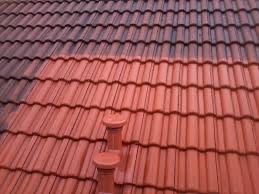 Częściowo wyczyszczony dach z czerwonej dachówki ceramicznej, widoczna różnica w kolorze między czystą a zabrudzoną powierzchnią, dwa kominki wentylacyjne na pierwszym planie.