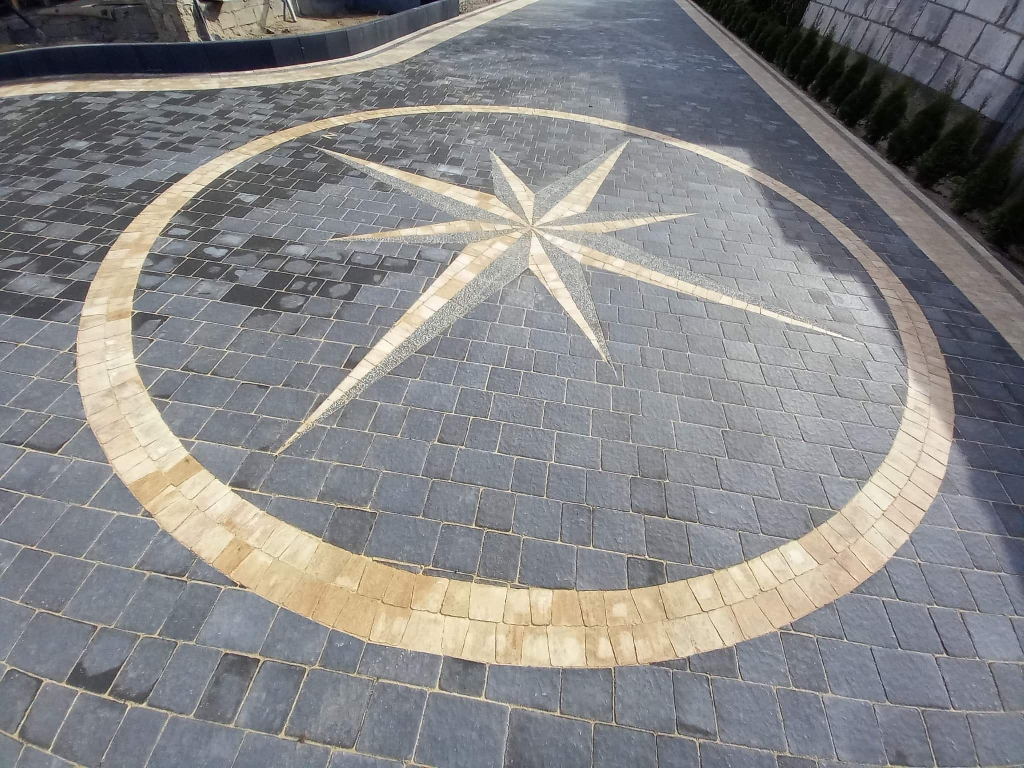 Ułożona kostka brukowa w szarym kolorze z dekoracyjnym wzorem rozety w odcieniach beżu i szarości, tworząca unikalny wzór na podjeździe.