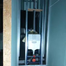 Stelaż podtynkowy Grohe zamontowany w konstrukcji z profili stalowych, z widocznymi fragmentami instalacji wodnej i kanalizacyjnej, przygotowany do zabudowy płytami gipsowo-kartonowymi.