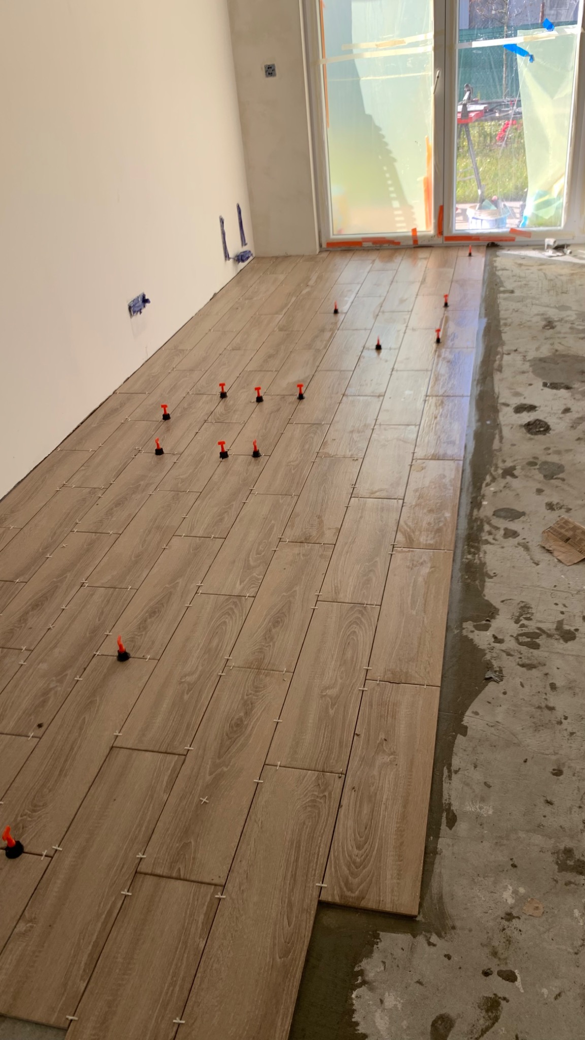 Układanie płytek podłogowych imitujących drewno, z użyciem poziomujących klipsów i klinów, widoczne niedociągnięcia na podłożu.