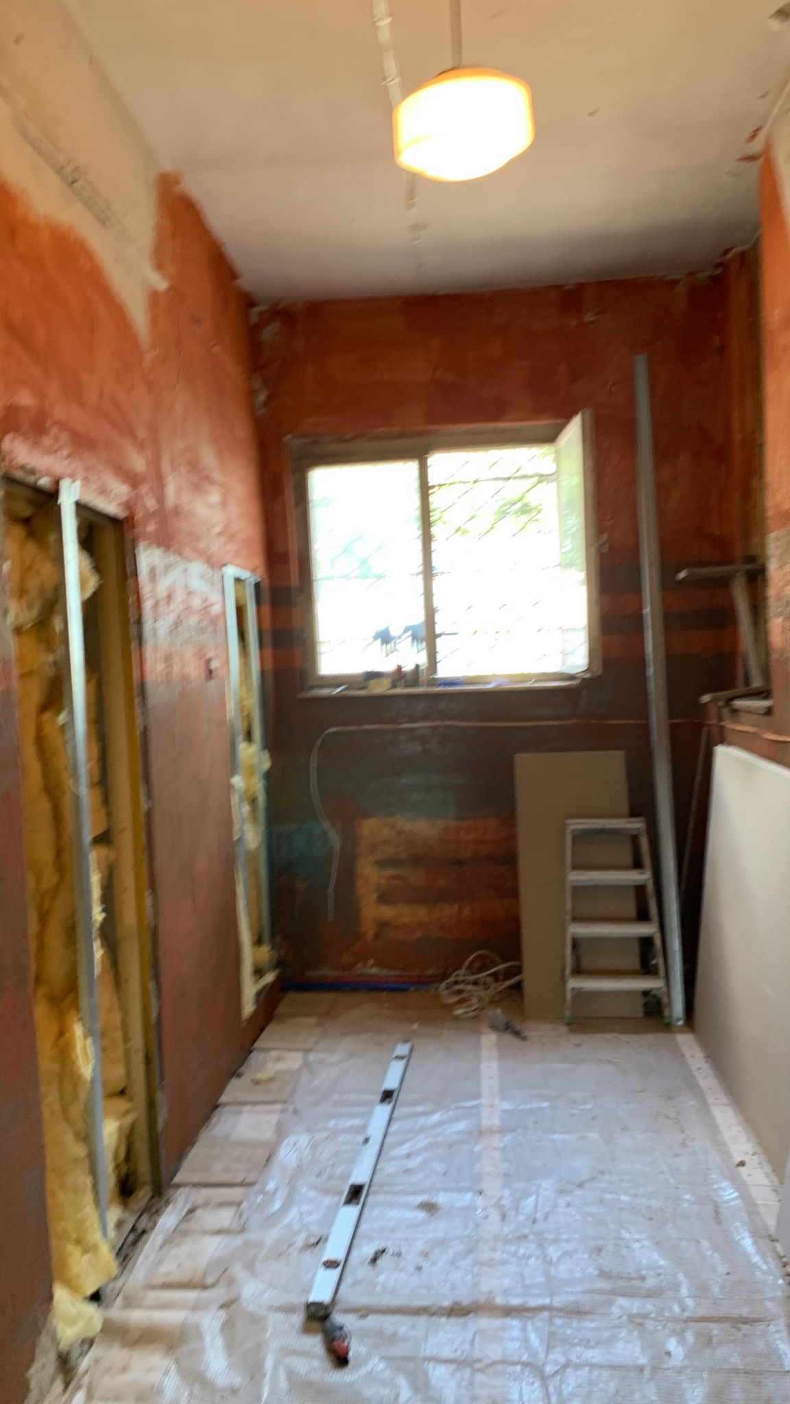 Wnętrze w trakcie prac przygotowawczych do wykończenia: odsłonięte ściany z instalacją, poziomica na podłodze zabezpieczonej folią, drabina oparta o ścianę, widoczne płyty gipsowe.