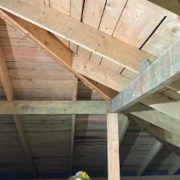 Konstrukcja drewniana poddasza z widoczną izolacją w rolce, widok od dołu, drewno surowe, metalowe łączniki.