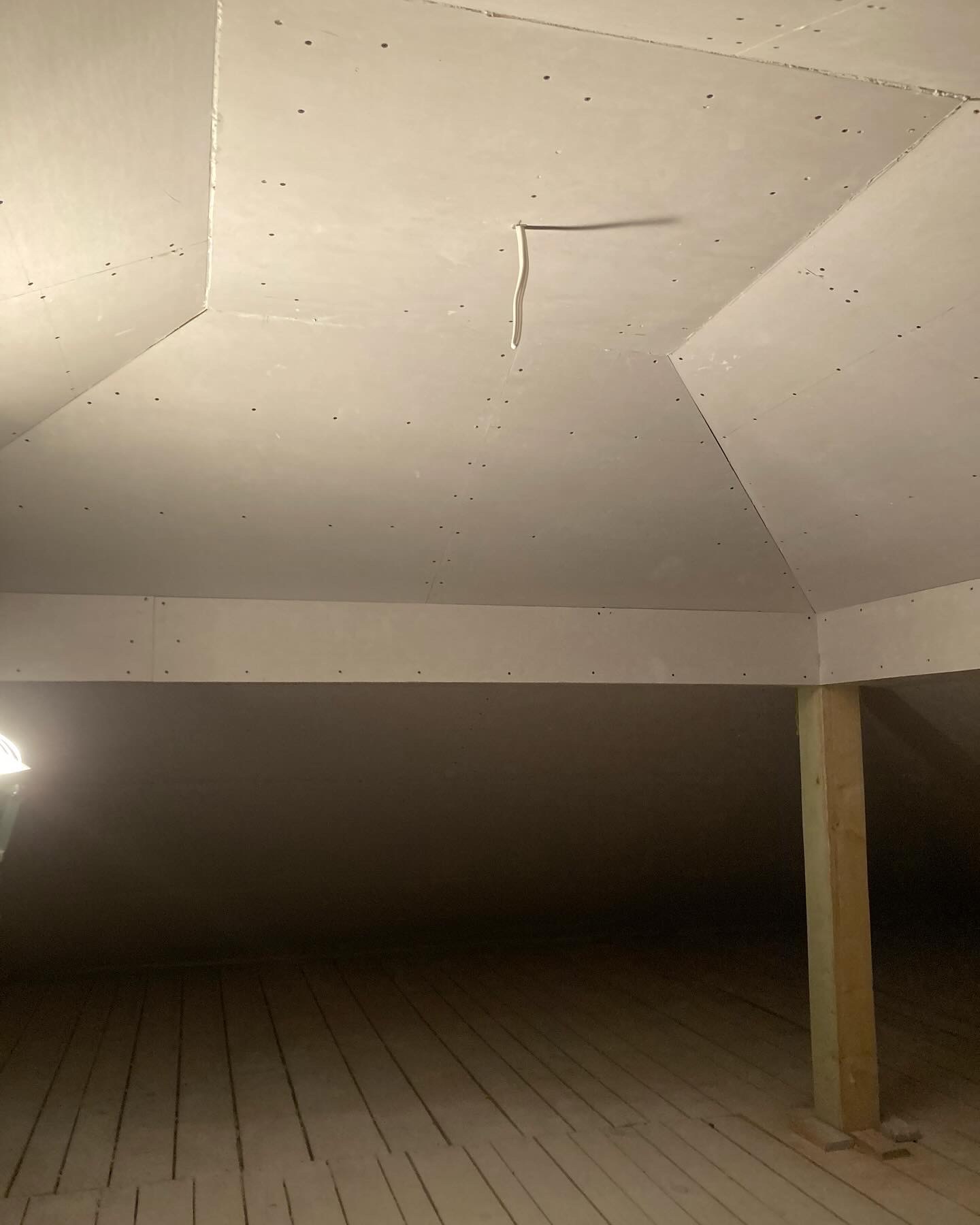 Poddasze w trakcie montażu płyt kartonowo-gipsowych, widoczne łączenia płyt i wystający kabel elektryczny, drewniana podłoga i konstrukcja wsporcza.
