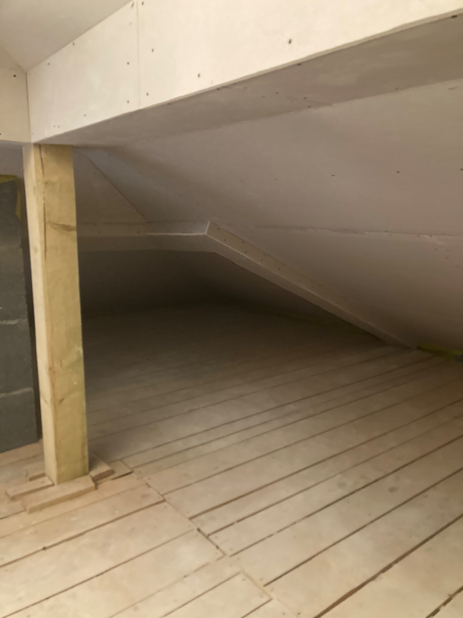 Poddasze w trakcie prac wykończeniowych: widoczne płyty kartonowo-gipsowe na skosach dachu, drewniana konstrukcja wsporcza i surowa drewniana podłoga z desek.