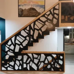 Schody drewniane z ażurową, geometryczną balustradą w kolorze czarnym, widok na turkusową ścianę z białymi drzwiami i kuchnię w tle.