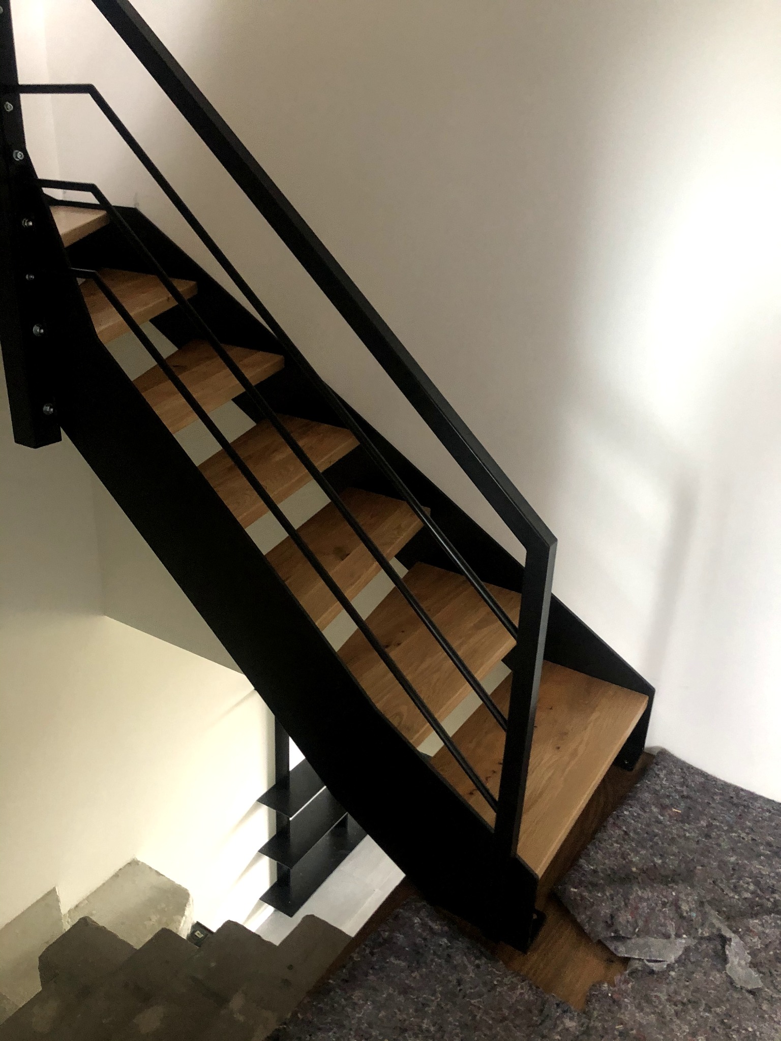 Nowoczesne schody metalowe z drewnianymi stopniami, widok z góry, zabezpieczone podłoże przed zabrudzeniem.