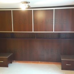 Infoduo Spółka z Ograniczoną Odpowiedzialnością - Zabudowa ściany z szafkami przesuwnymi i szafkami nocnymi w kolorze ciemnego drewna, na ścianie żółta farba, widoczne niedoskonałości wykończenia, na zdjęciu widoczny znak wodny.