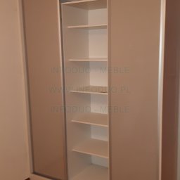 Infoduo Spółka z Ograniczoną Odpowiedzialnością - Szafa wnękowa z przesuwnymi drzwiami w kolorze beżowym, z widocznymi półkami w środkowej części, na tle parkietu ułożonego w jodełkę.