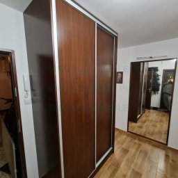 Infoduo Spółka z Ograniczoną Odpowiedzialnością - Wysoka szafa przesuwna z drewnopodobnymi frontami i jasnymi obramowaniami, widoczna w przedpokoju z lustrem i drewnianą podłogą.