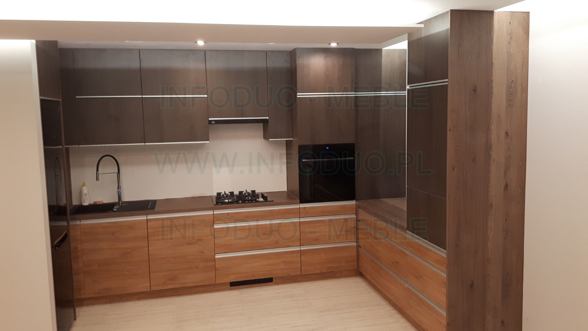 Nowoczesna zabudowa kuchenna z drewnianymi frontami w odcieniach brązu, z czarnym zlewem, płytą gazową i piekarnikiem, oświetleniem punktowym i minimalistycznymi uchwytami.