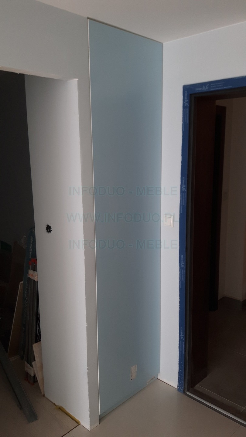 Narożna zabudowa z błękitnymi frontami, widoczna w trakcie montażu, z elementami konstrukcyjnymi i narzędziami w tle oraz logo firmy na powierzchni.