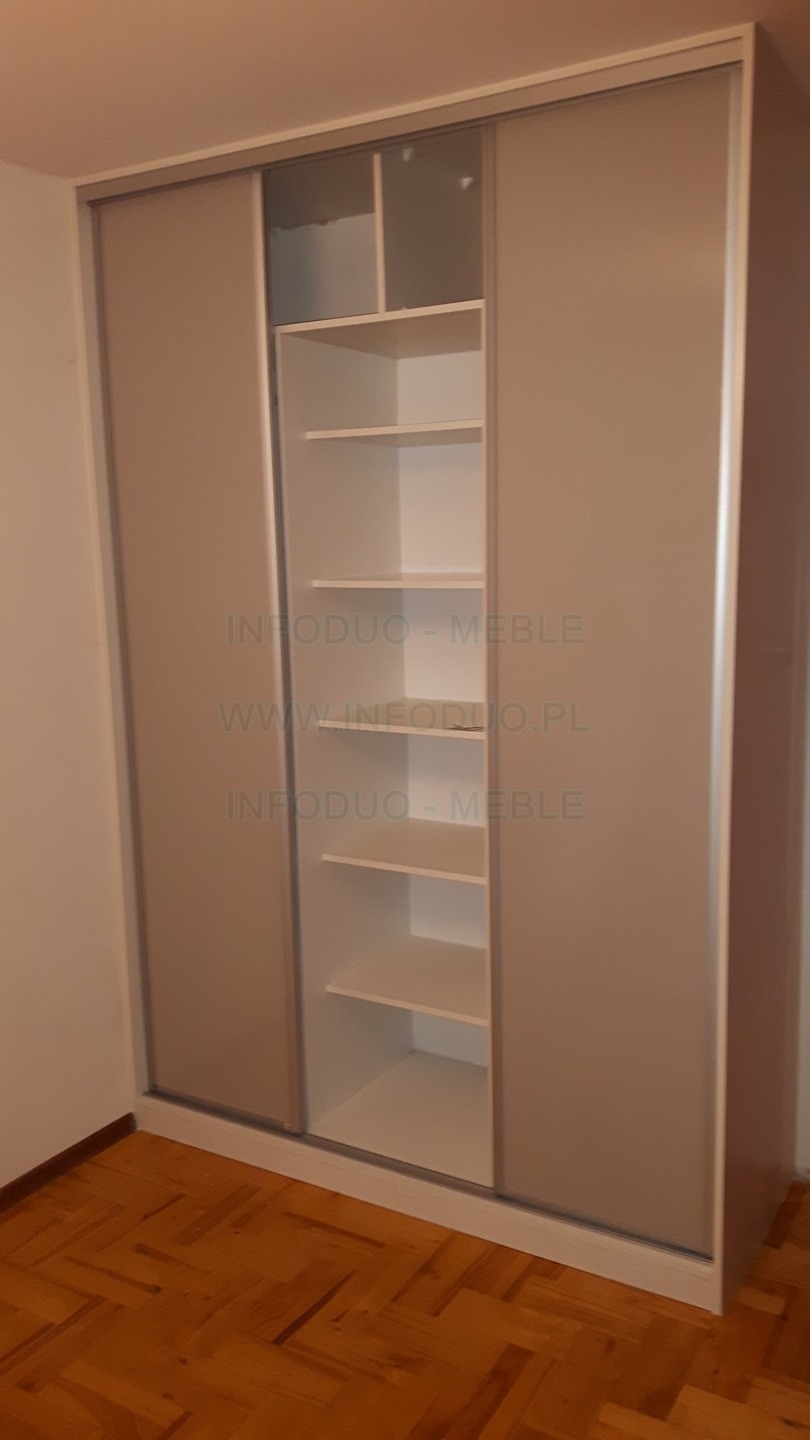 Szafa wnękowa z przesuwnymi drzwiami w kolorze beżowym, z widocznymi półkami w środkowej części, na tle parkietu ułożonego w jodełkę.