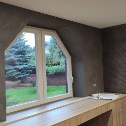 Kobar - Pokój na poddaszu z trapezoidalnym oknem, szarą ścianą o fakturze betonu, drewnianym blatem pod oknem i tapetą w stylu vintage z motywem koła na przeciwległej ścianie.