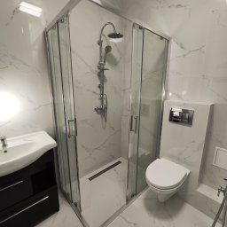 Kobar - Nowoczesna łazienka z kabiną prysznicową z chromowanymi profilami, umywalką z szafką w kolorze czarnym i podwieszaną toaletą, wykończona białymi płytkami imitującymi marmur.