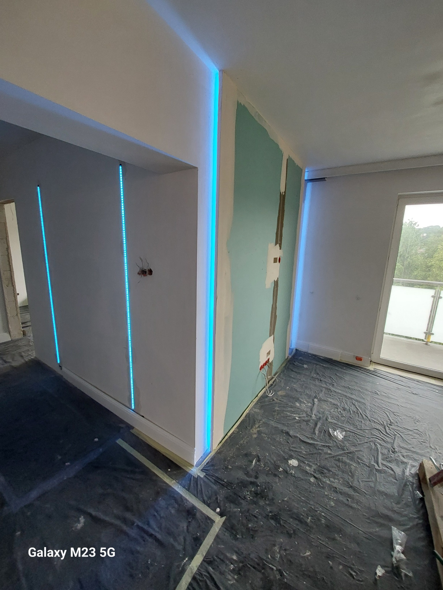 Wnętrze w trakcie prac wykończeniowych z podświetleniem LED: ściany z płyt gipsowo-kartonowych, zabezpieczona folią podłoga, widoczne przewody elektryczne.