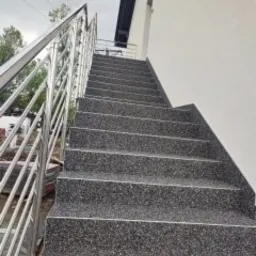 Zewnętrzne schody z szarego lastryko prowadzące do budynku, zabezpieczone metalową balustradą ze stali nierdzewnej, widok z dołu.