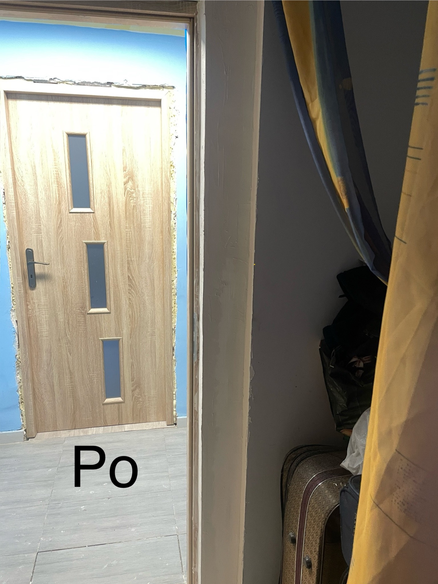 Montaż drzwi wewnętrznych z trzema okienkami, widoczne szpary wypełnione pianką montażową, niebieska ściana w tle.