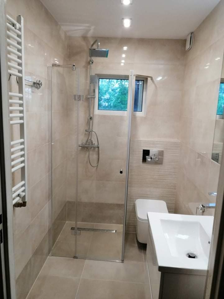 Nowoczesna łazienka z beżowymi płytkami, kabiną prysznicową typu walk-in z odpływem liniowym, grzejnikiem drabinkowym i minimalistyczną umywalką.