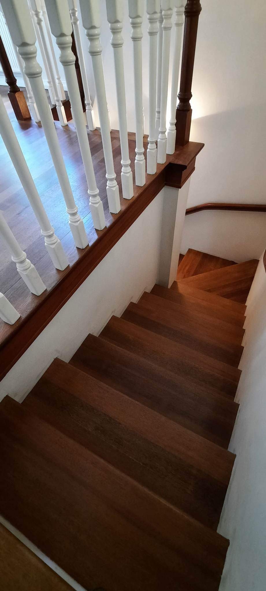 Odnowione drewniane schody z białymi balustradami i mahoniową poręczą, widok z góry.