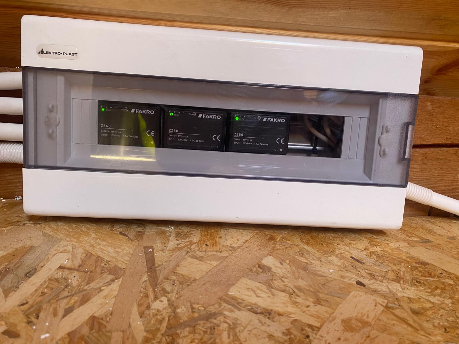 Biała skrzynka elektryczna Elektro-Plast z trzema modułami zasilającymi Fakro ZZ60, zamontowana na drewnianej płycie OSB.