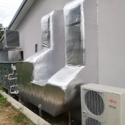 Zewnętrzny widok rekuperatora z izolacją termiczną i jednostką klimatyzacyjną Fujitsu Airstage, umieszczonych przy ścianie budynku.