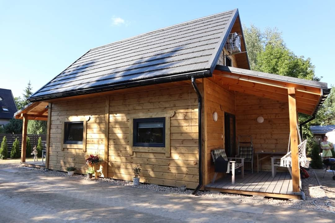 Zewnętrzny widok nowo wybudowanego, drewnianego domu letniskowego z szarym dachem, czarnymi rynnami i małym tarasem.
