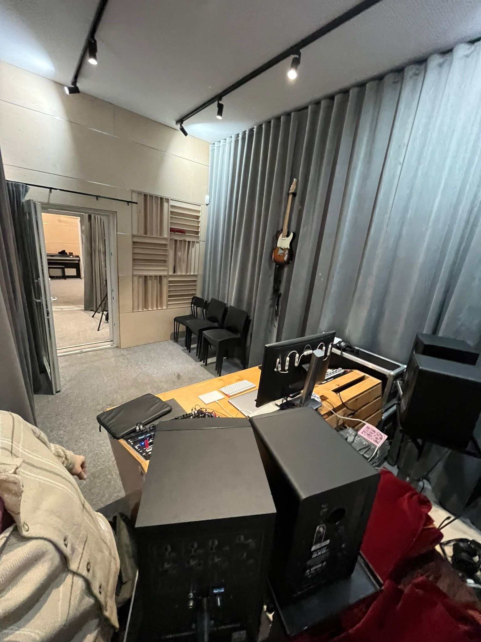 Wnętrze studia nagrań z biurkiem, monitorem, głośnikami, gitarą na ścianie i panelami akustycznymi na ścianach.