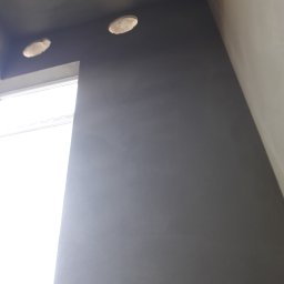 BARTO-TYNK - Świeżo położona szara gładź na ścianie w Pałecznicy, z widocznymi otworami na oświetlenie sufitowe i oknem po lewej stronie, uchwycona pod kątem z dołu.