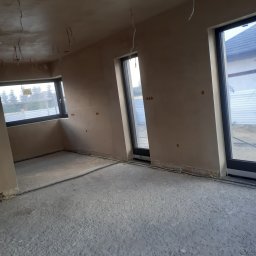 BARTO-TYNK - Surowe wnętrze po tynkowaniu maszynowym, widoczne wyprowadzone kable elektryczne, trzy okna z czarnymi ramami i szary betonowy podkład podłogowy.